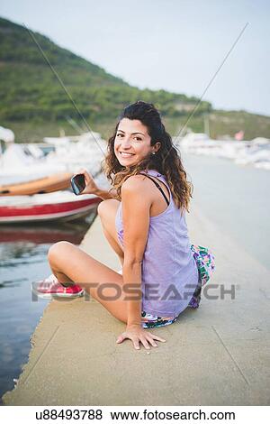 Stock Photo - Woman at coast, with smartphone, looking at camera. Fotosearch