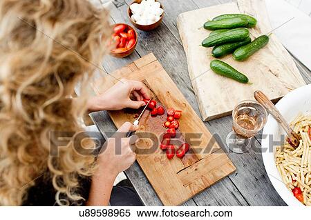 Stock Photography - Woman chopping tomatoes on wooden chopping board, high angle. Fotosearch