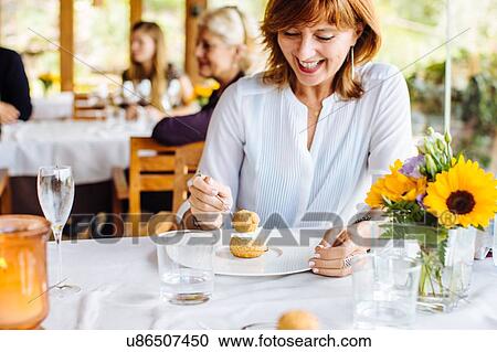 Stock Image - Woman eating profiterole with whipped cream in restaurant, Italy. Fotosearch