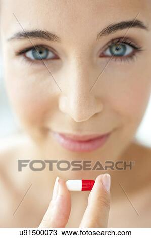 Stock Image - Woman holding a red and white capsule. Fotosearch