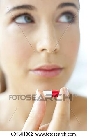 Stock Image - Woman holding a red and white capsule. Fotosearch
