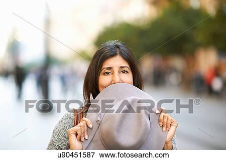 Stock Photo - Woman holding hat over mouth on street. Fotosearch
