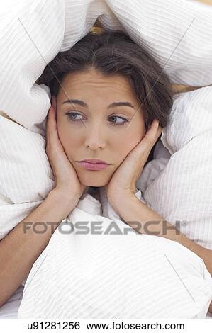 Stock Photograph - Woman in bed with hands on chin. Fotosearch