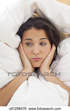 Stock Photograph - Woman in bed with hands on chin. Fotosearch