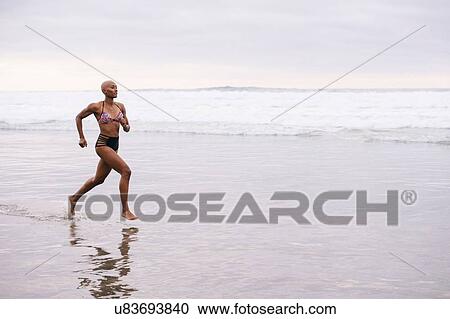 Stock Image - Woman in bikini jogging on beach. Fotosearch