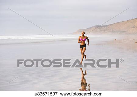 Stock Photo - Woman in bikini jogging on beach. Fotosearch