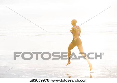 Stock Photograph - Woman in bikini jogging on beach. Fotosearch