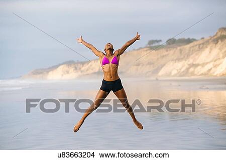 Picture - Woman in bikini jumping on beach. Fotosearch