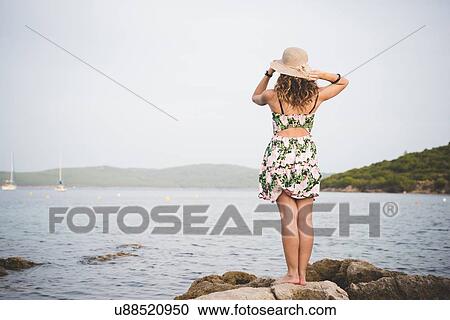 Stock Image - Woman looking out to sea, wearing hat, rear view. Fotosearch