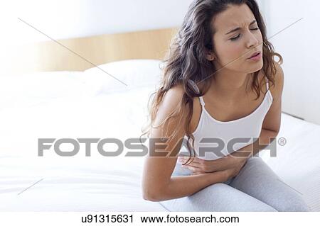 Stock Image - Woman on bed with cramps. Fotosearch