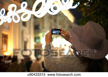 Stock Photography - Woman photographing decorative lights in street, Seville, Spain. Fotosearch
