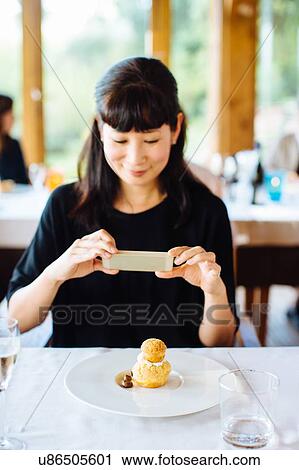 Stock Image - Woman photographing profiterole with whipped cream in restaurant, Italy. Fotosearch