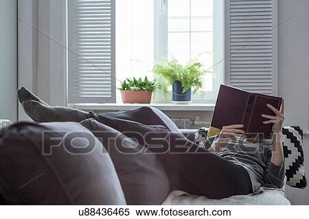 Woman reclining on living room sofa reading a book View Large Photo Image Stock Photography - Woman reclining on living room sofa reading a book. Fotosearch