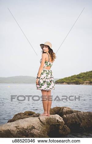 Stock Photograph - Woman standing on rocks by the sea. Fotosearch