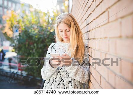 Woman texting on smartphone, against brick wall View Large Photo Image Stock Image - Woman texting on smartphone, against brick wall. Fotosearch