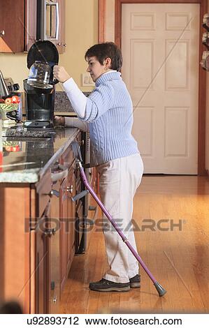 Stock Image - Woman using crutches in her kitchen. Fotosearch