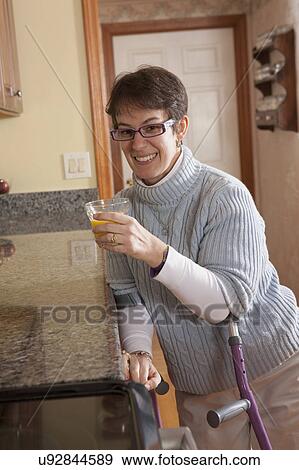 Stock Photo - Woman using crutches in her kitchen. Fotosearch