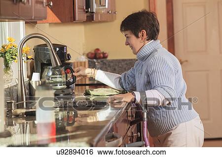 Stock Photograph - Woman using crutches in her kitchen. Fotosearch