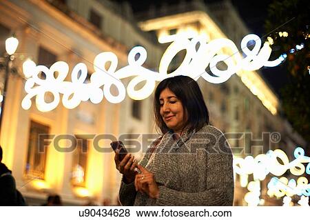 Stock Photo - Woman using smartphone, decorative lights in background, Seville, Spain. Fotosearch
