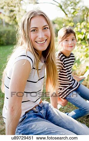 Stock Image - Woman with long blond hair, daughter in background. Fotosearch