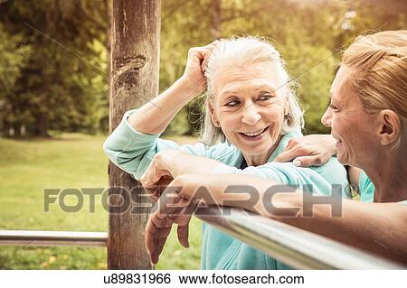 Women in park leaning against metal bar face to face smiling View Large Photo Image Stock Photograph - Women in park leaning against metal bar face to face smiling. Fotosearch