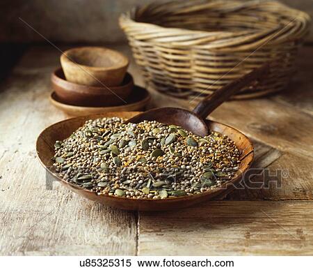 Stock Photography - Wooden bowl with pumpkin seeds, golden linseeds on hemp seeds on wooden table. Fotosearch
