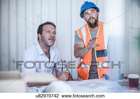 Stock Image - Worker and construction foreman meeting at desk in portable cabin. Fotosearch