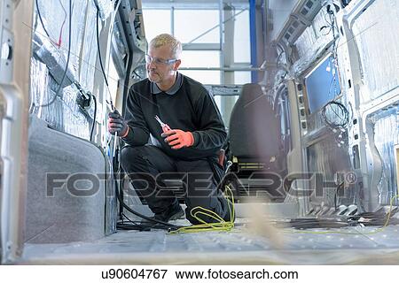 Stock Photo - Worker fitting electrics on motorhome production line. Fotosearch