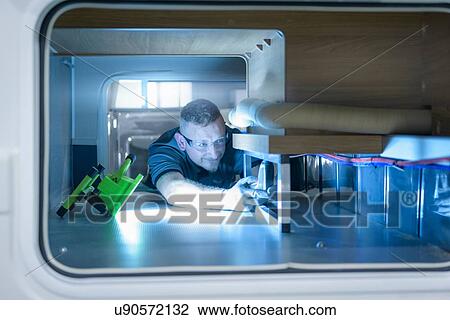 Stock Image - Worker fitting parts on vehicle on motorhome production line. Fotosearch