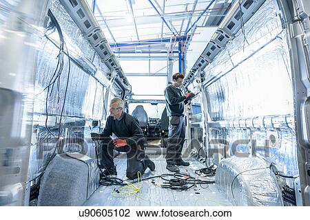 Stock Image - Workers fitting electrics on motorhome production line. Fotosearch