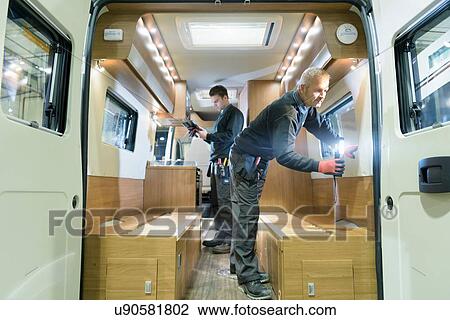Stock Image - Workers inspecting vehicle on motorhome production line. Fotosearch