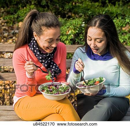 Young adult female twins sitting on park bench chatting and eating lunch View Large Photo Image Stock Image - Young adult female twins sitting on park bench chatting and eating lunch. Fotosearch