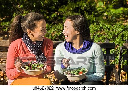 Young adult female twins sitting on park bench eating lunch View Large Photo Image Stock Image - Young adult female twins sitting on park bench eating lunch. Fotosearch