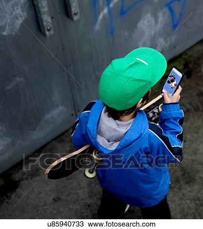 Stock Image - Young boy looking at photo of skateboarder on smartphone. Fotosearch