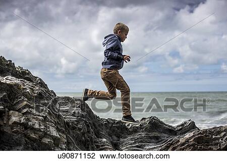 Stock Image - Young boy playing on rocks on beach. Fotosearch