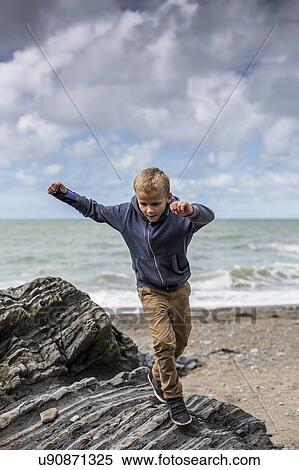 Stock Photography - Young boy playing on rocks on beach. Fotosearch