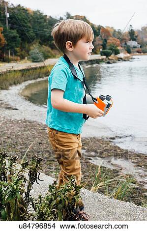 Picture - "Young boy standing beside lake, holding binoculars". Fotosearch