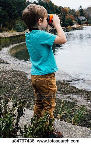 "Young boy standing beside lake, looking through binoculars" View Large Photo Image Stock Photograph - "Young boy standing beside lake, looking through binoculars". Fotosearch
