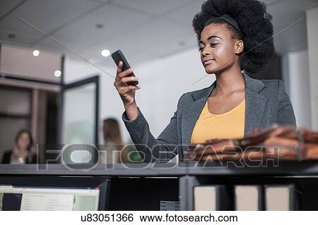 Stock Photograph - Young businesswoman reading smartphone text at office reception. Fotosearch