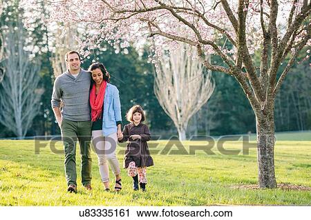Stock Image - Young couple and daughter strolling in spring park. Fotosearch
