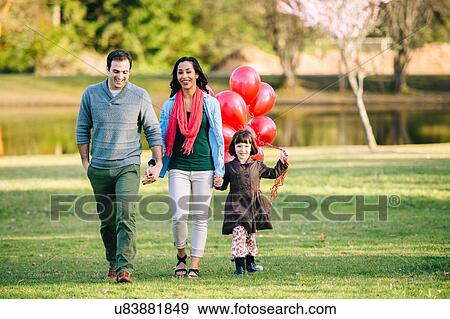 Stock Photo - Young couple and daughter with bunch of red balloons strolling in park. Fotosearch