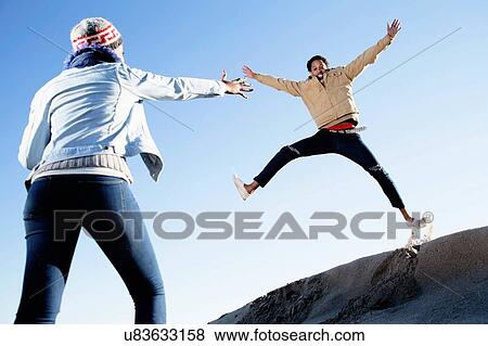 Stock Photo - "Young couple fooling around on beach in winter, young man jumping". Fotosearch
