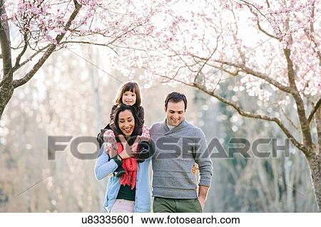 Stock Image - Young couple giving daughter a shoulder carry in spring park. Fotosearch