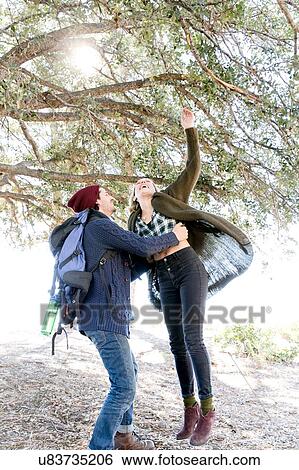 Stock Photograph - "Young couple in rural setting, fooling around, young woman trying to reach tree branch". Fotosearch