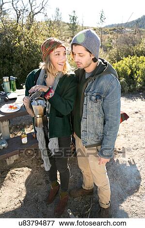 Stock Photo - "Young couple in rural setting, holding coffee pot by picnic bench". Fotosearch