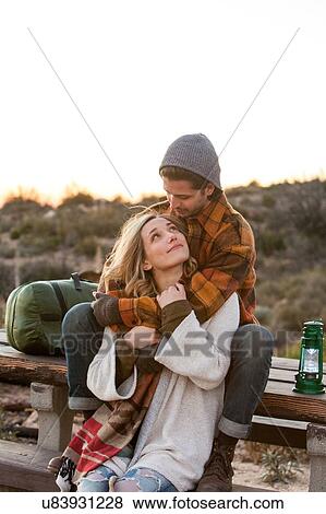 Stock Photo - "Young couple in rural setting, sitting on picnic bench, hugging". Fotosearch