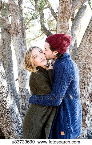 Stock Image - "Young couple in rural setting, young man kissing young woman on cheek". Fotosearch