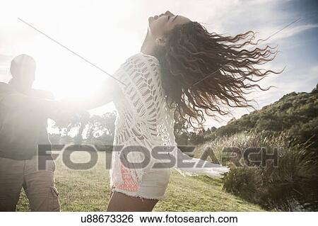 Stock Photograph - Young couple in sunlight holding hands throwing head back smiling. Fotosearch