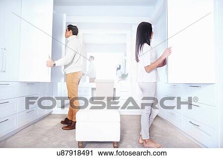 Stock Image - Young couple looking in bedroom closets. Fotosearch