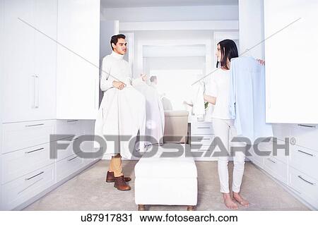 Stock Image - Young couple making decisions whilst getting ready in bedroom. Fotosearch